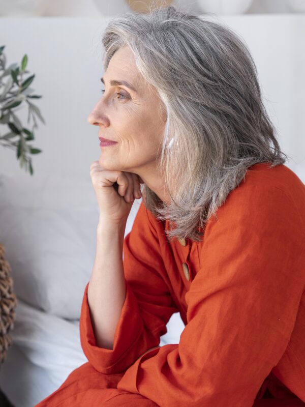 Donna anziana con capelli grigi al naturale guarda fuori dalla finestra