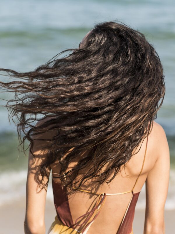 Ragazza di spalle al mare che sventola i capelli