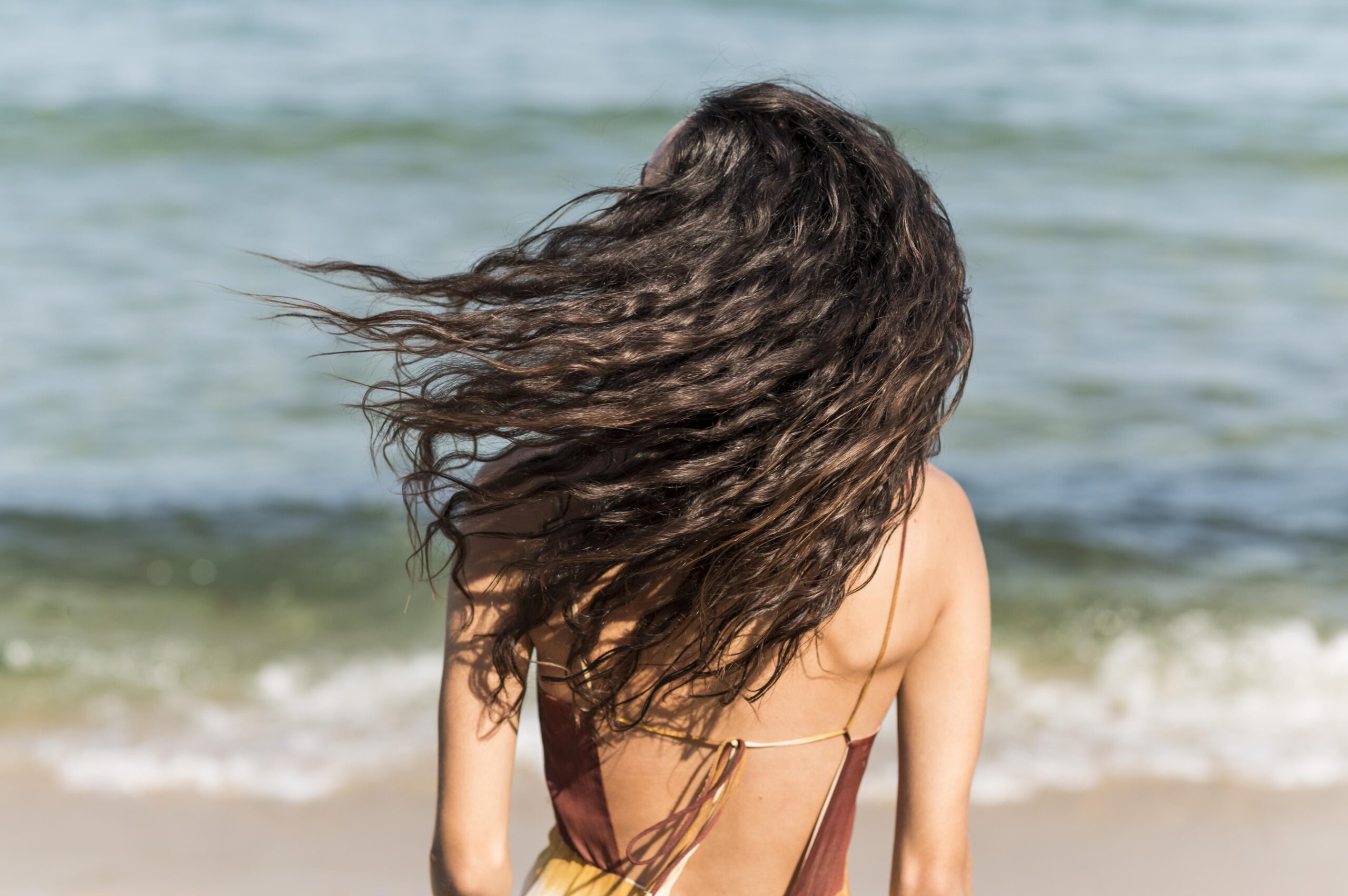 Ragazza di spalle al mare che sventola i capelli